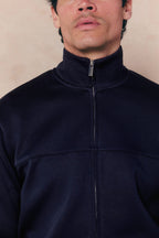 Man wearing a navy Luxe Zip Through Jacket with a high collar and silver zipper.