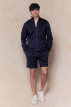 Man wearing a navy Luxe Zip Through Jacket and matching shorts, with a white t-shirt and sneakers.