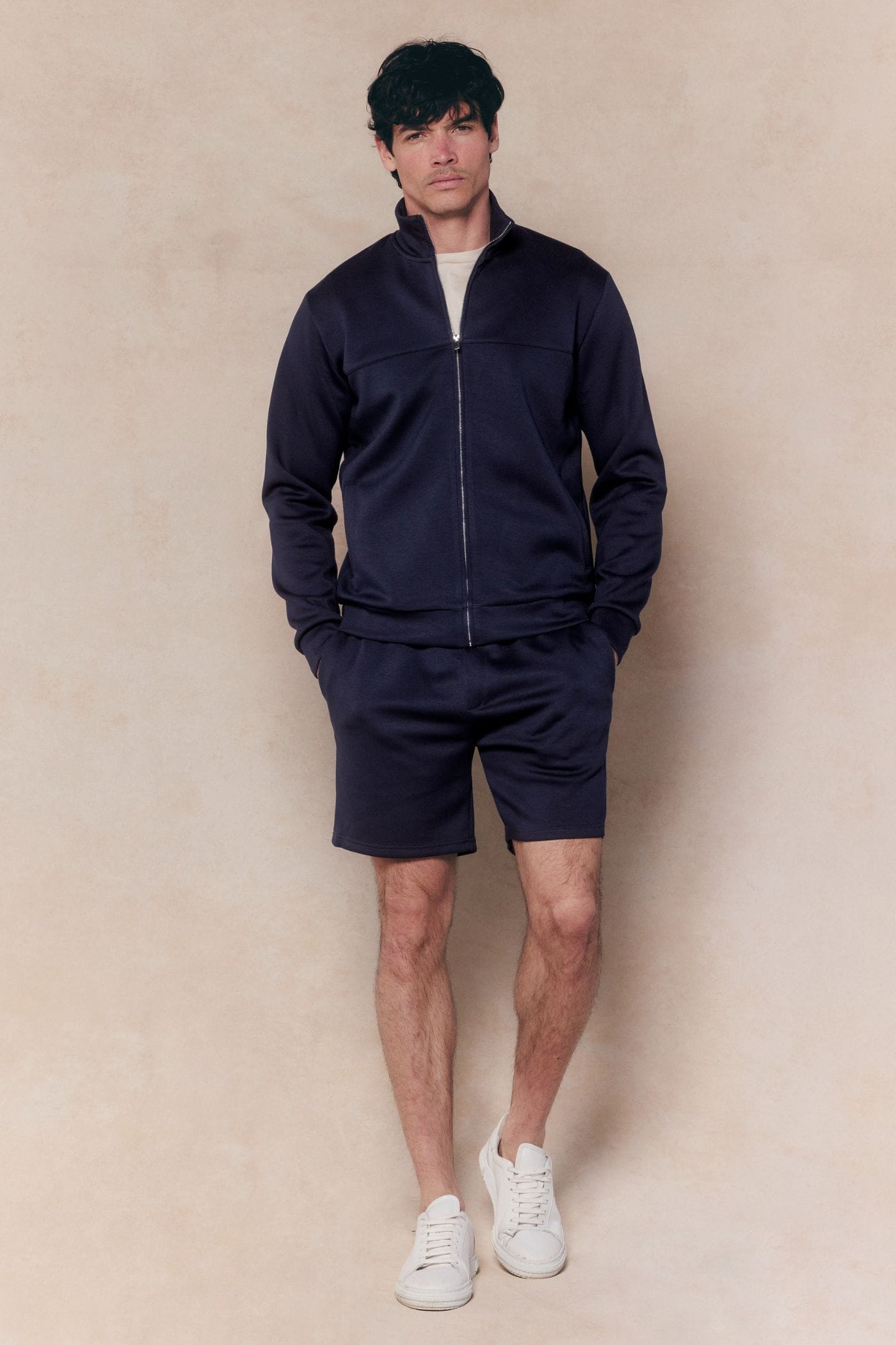 Man wearing a navy Luxe Zip Through Jacket and matching shorts, with a white t-shirt and sneakers.