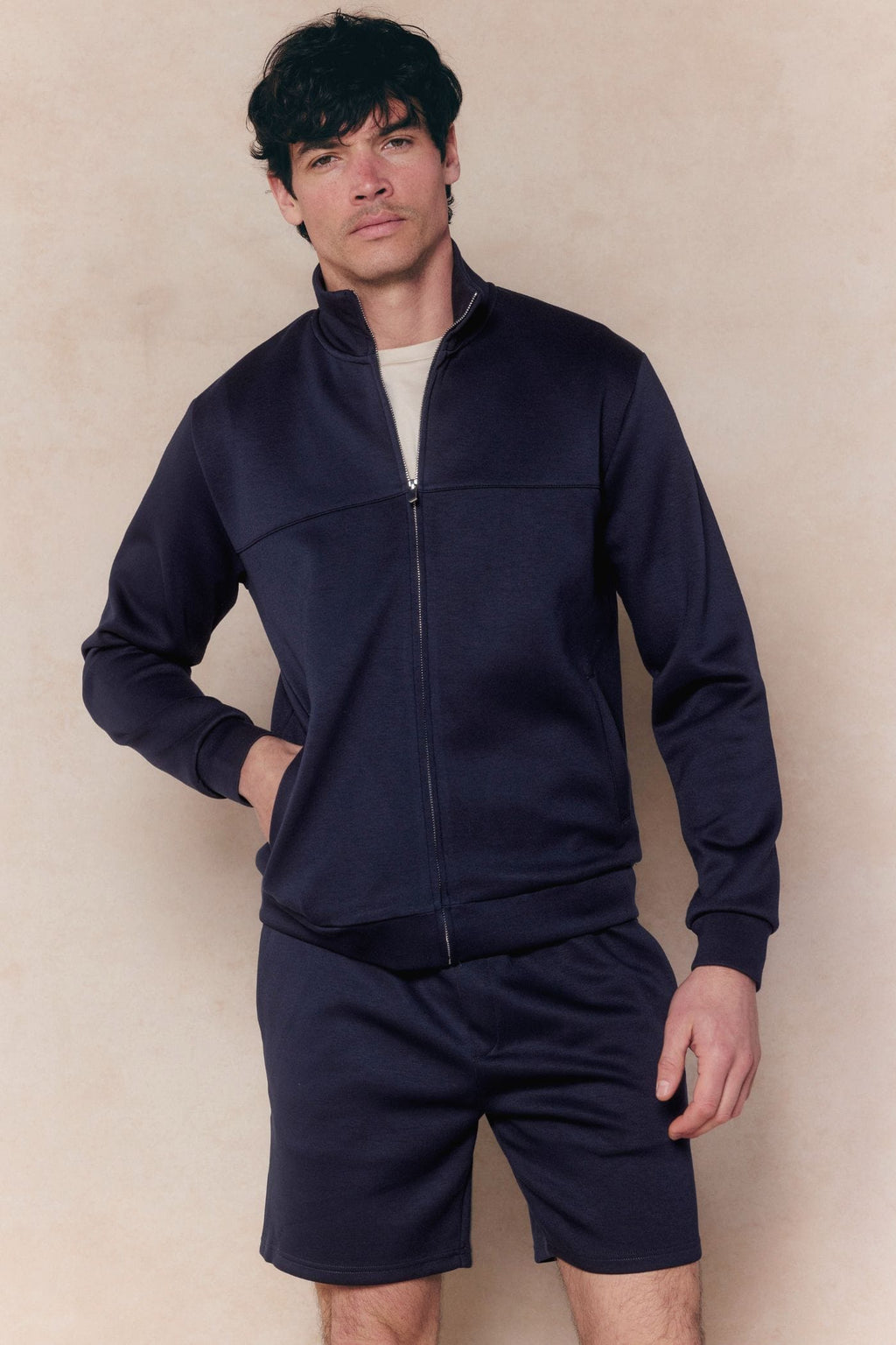 Man wearing a navy Luxe Zip Through Jacket and matching shorts, featuring a relaxed fit and soft, stretchy fabric.