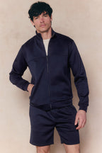 Man wearing a navy Luxe Zip Through Jacket and matching shorts, featuring a relaxed fit and soft, stretchy fabric.