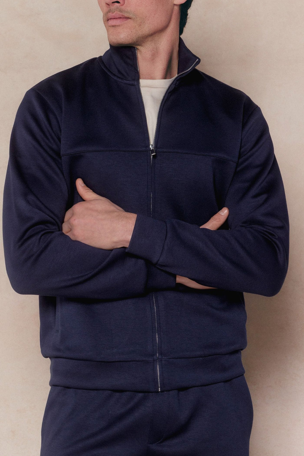 Man in a navy Luxe Zip Through Jacket with a stand collar and silver zipper, arms crossed.