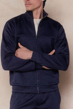 Man in a navy Luxe Zip Through Jacket with a stand collar and silver zipper, arms crossed.