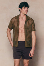 Man in a brown Marcelo short sleeve lace shirt, open over his chest, paired with dark shorts.