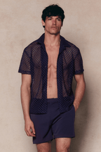 Man in a navy Marcelo short sleeve lace shirt and matching shorts, unbuttoned to reveal his torso.