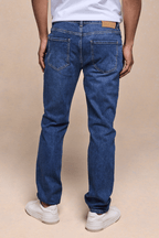 Man wearing Marco Washed Jean in mid wash indigo, showing back pockets, leather patch, and white sneakers.
