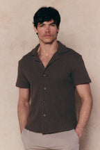 Man wearing a brown Marcos patterned waffle short sleeve shirt with an open collar and light pants.