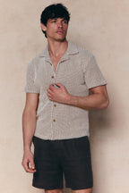 Man in a white and brown patterned waffle short sleeve shirt with an open collar and dark shorts.