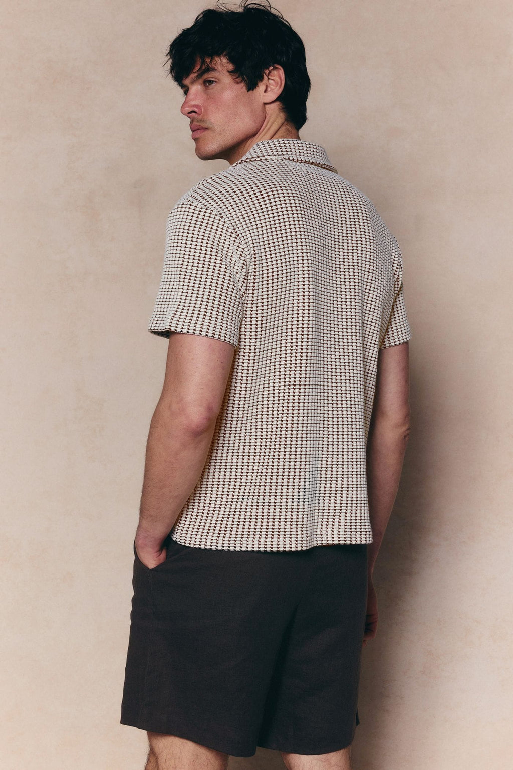Man in Marcos white/brown patterned waffle short sleeve shirt with open collar and dark shorts.