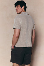 Man in Marcos white/brown patterned waffle short sleeve shirt with open collar and dark shorts.