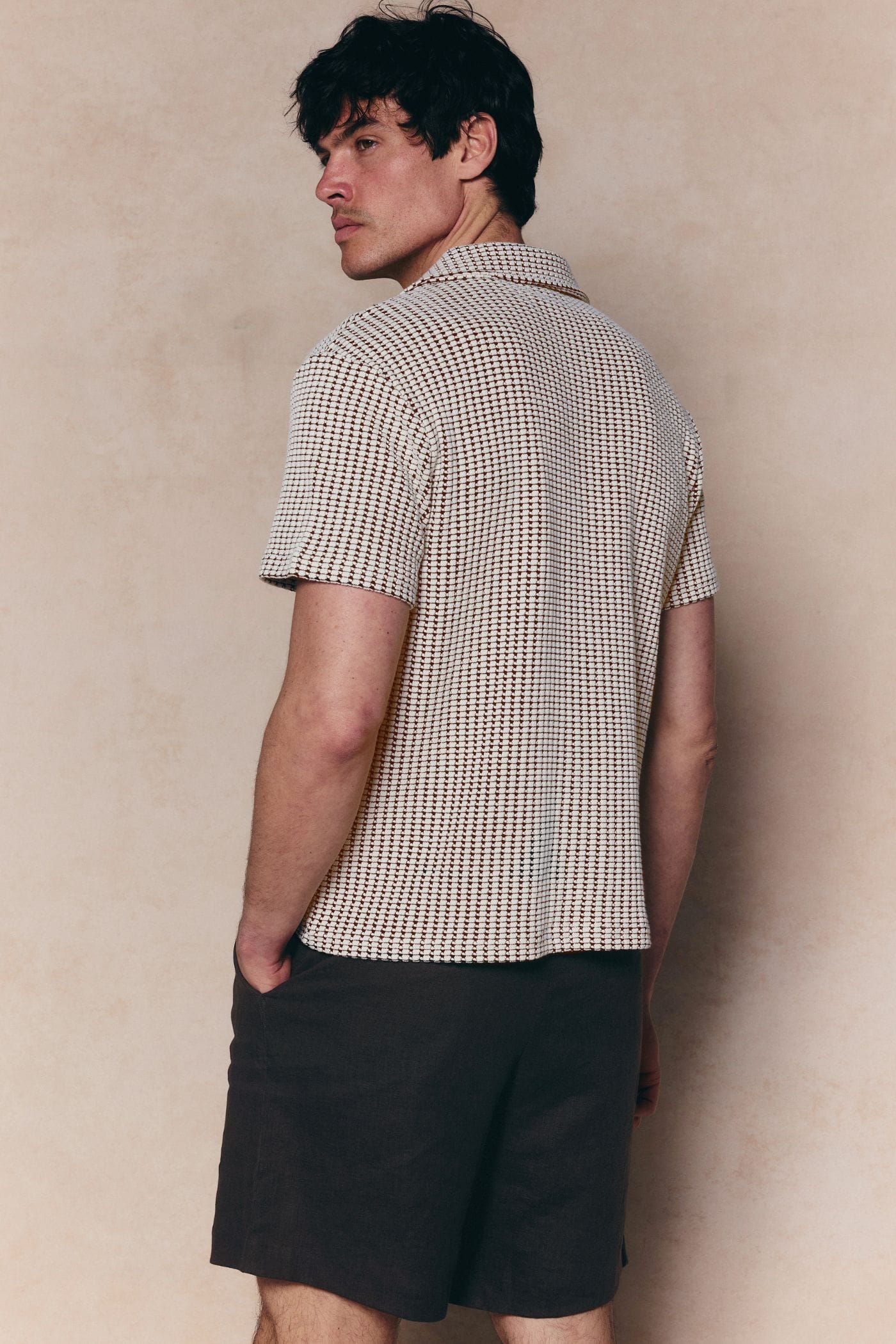 Man in Marcos white/brown patterned waffle short sleeve shirt with open collar and dark shorts.