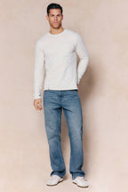 Man wearing Mason Relaxed Fit Midwash Indigo Jeans with a tan leather back patch and a cream long-sleeve shirt.