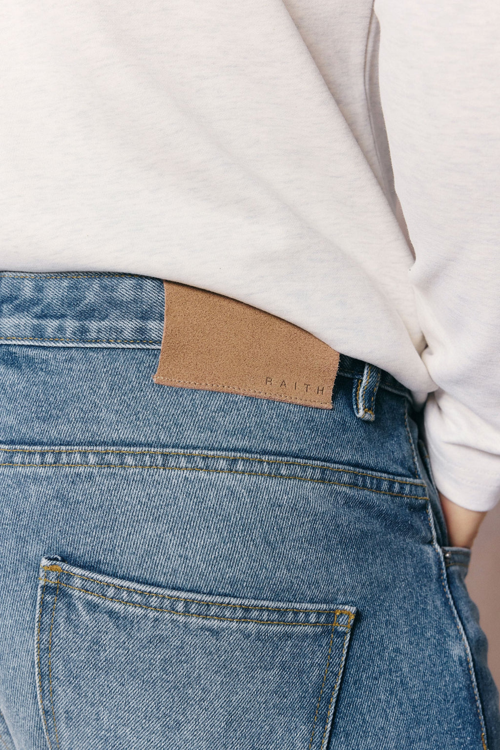 Close-up of Mason Relaxed Fit Jeans in midwash indigo 100% cotton denim with tan leather back patch.