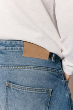 Close-up of Mason Relaxed Fit Jeans in midwash indigo 100% cotton denim with tan leather back patch.