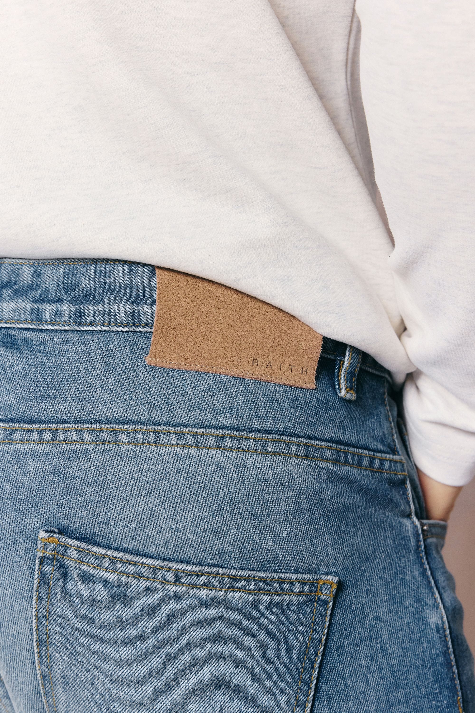 Close-up of Mason Relaxed Fit Jeans in midwash indigo 100% cotton denim with tan leather back patch.