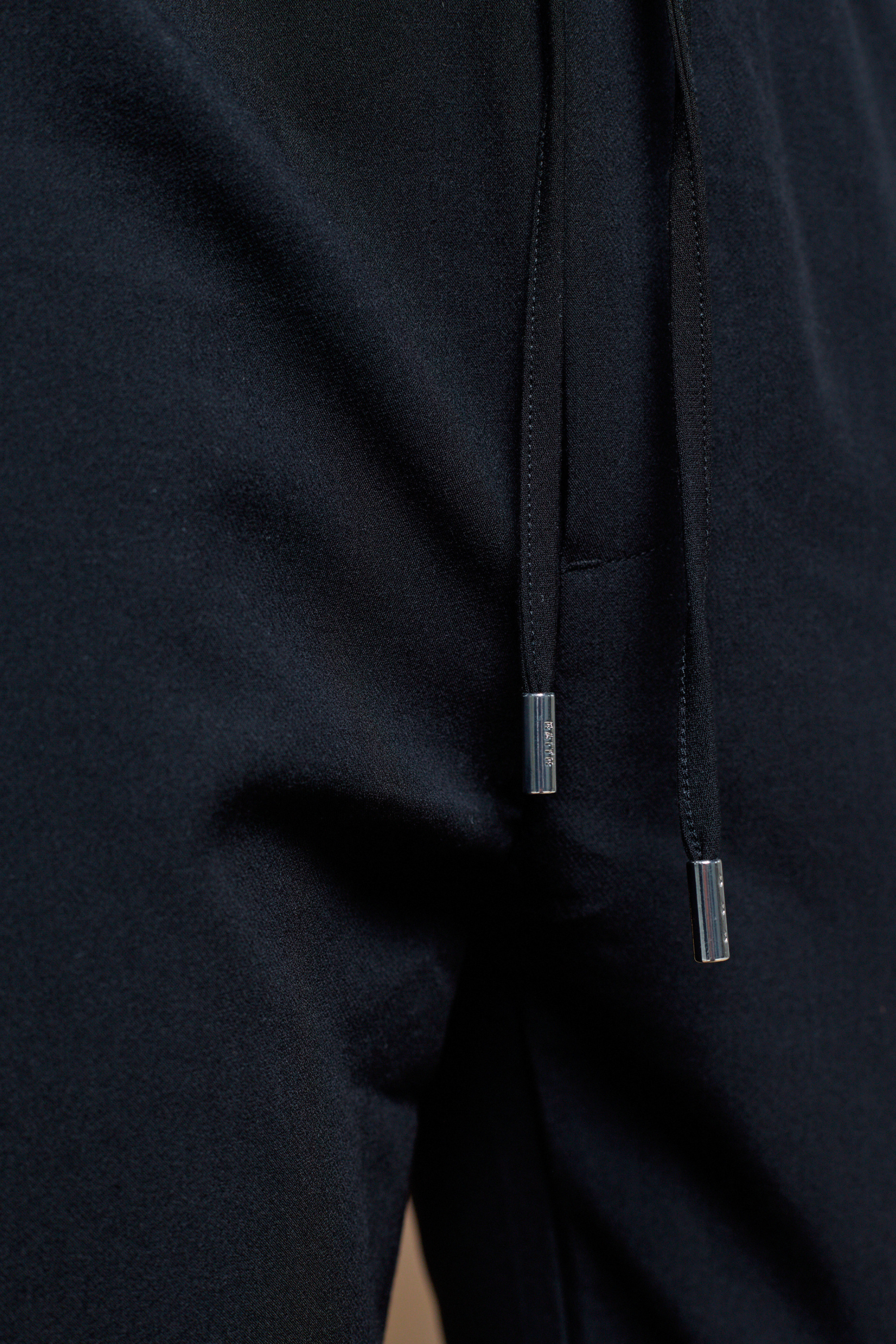 Close-up of black Mateo Tapered Trouser with elasticated drawcord waistband and silver metal tips.