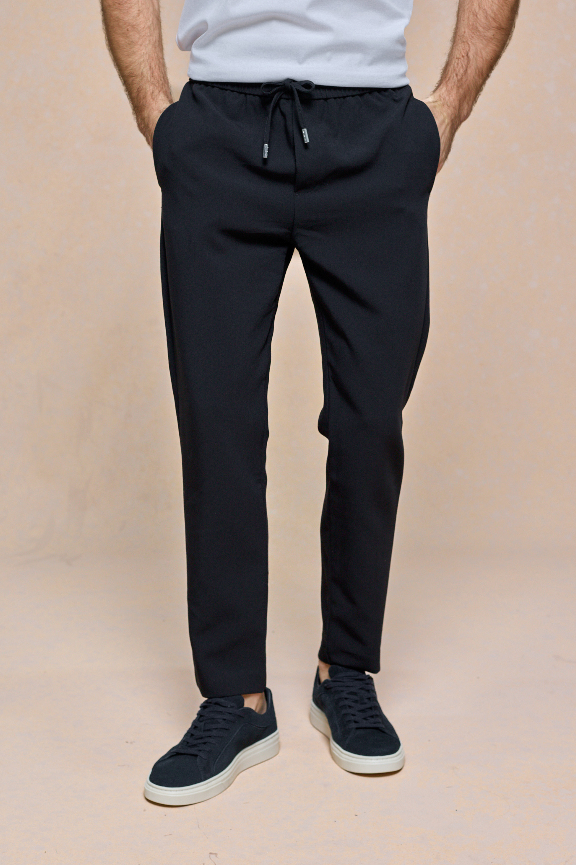 Black Mateo Tapered Trouser with elasticated drawcord waistband, worn by a person with hands in pockets.