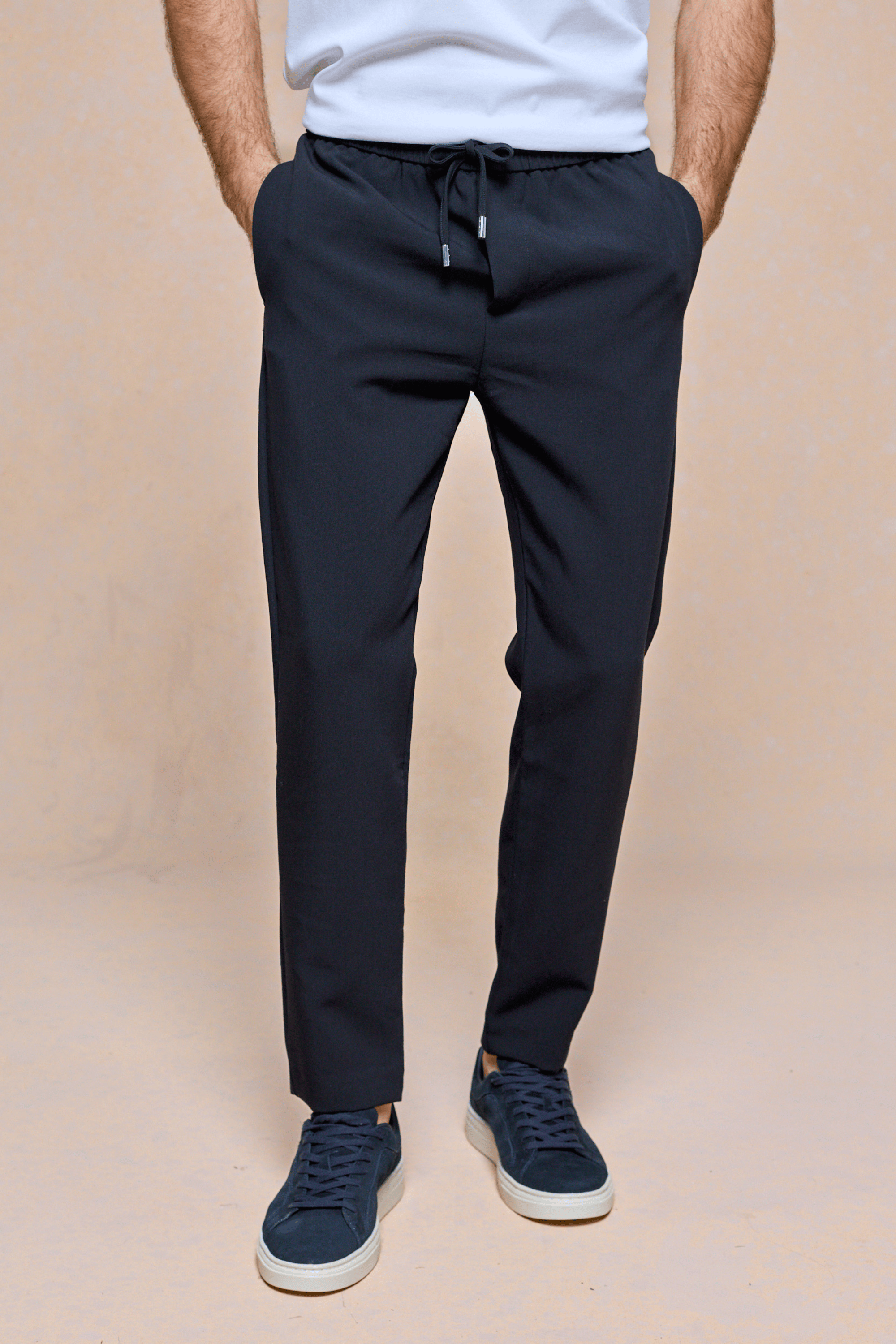 Dark navy Mateo tapered trousers with elasticated drawcord waistband, worn by a man with hands in pockets.