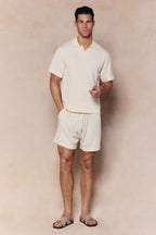 Man wearing an ecru Miguel Boucle Polo Shirt and matching shorts, with an open collar and textured fabric.