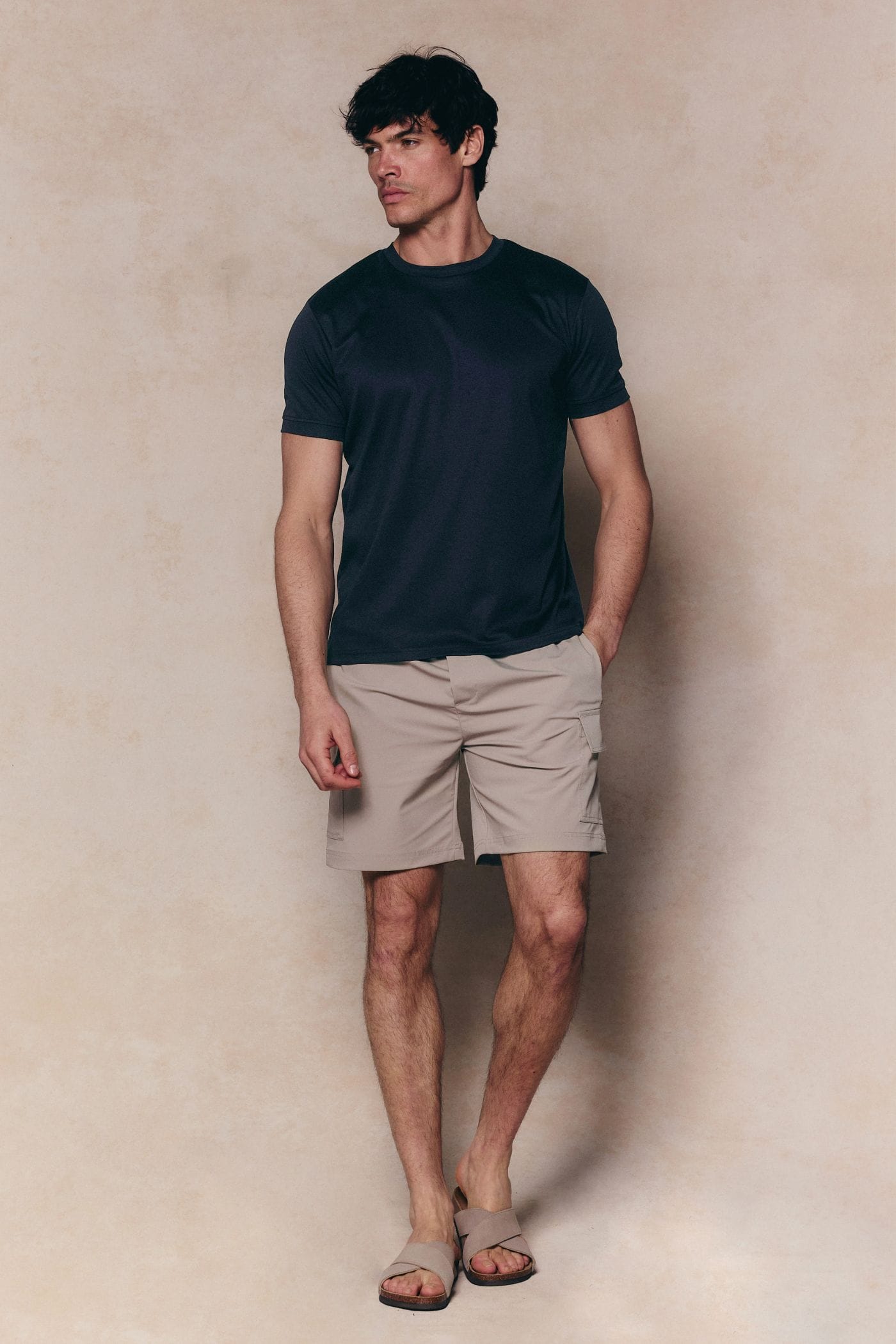 Man wearing beige Milo Cargo Tech Shorts with patch pockets and a navy t-shirt.