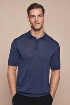 Man in a navy knitted short-sleeve polo with a half placket and ribbed sleeves, hands in pockets.