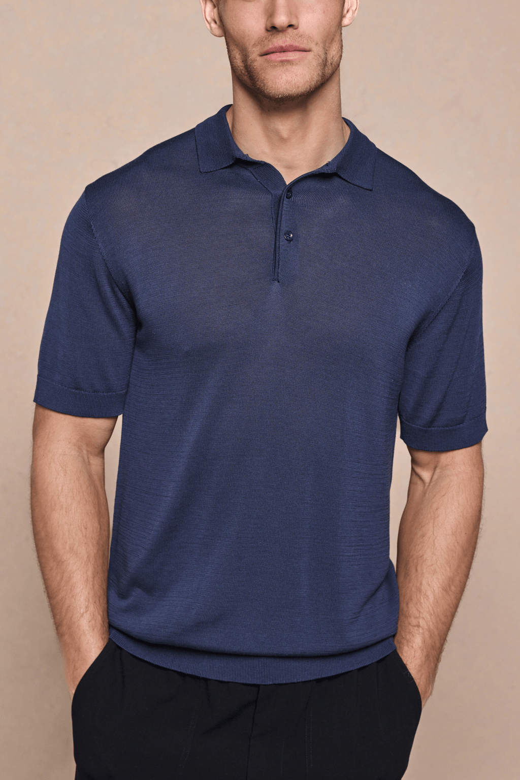 Man wearing a navy knitted short sleeve polo with a half placket and ribbed details.