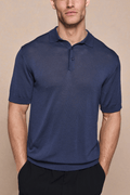 Man wearing a navy knitted short sleeve polo with a half placket and ribbed details.