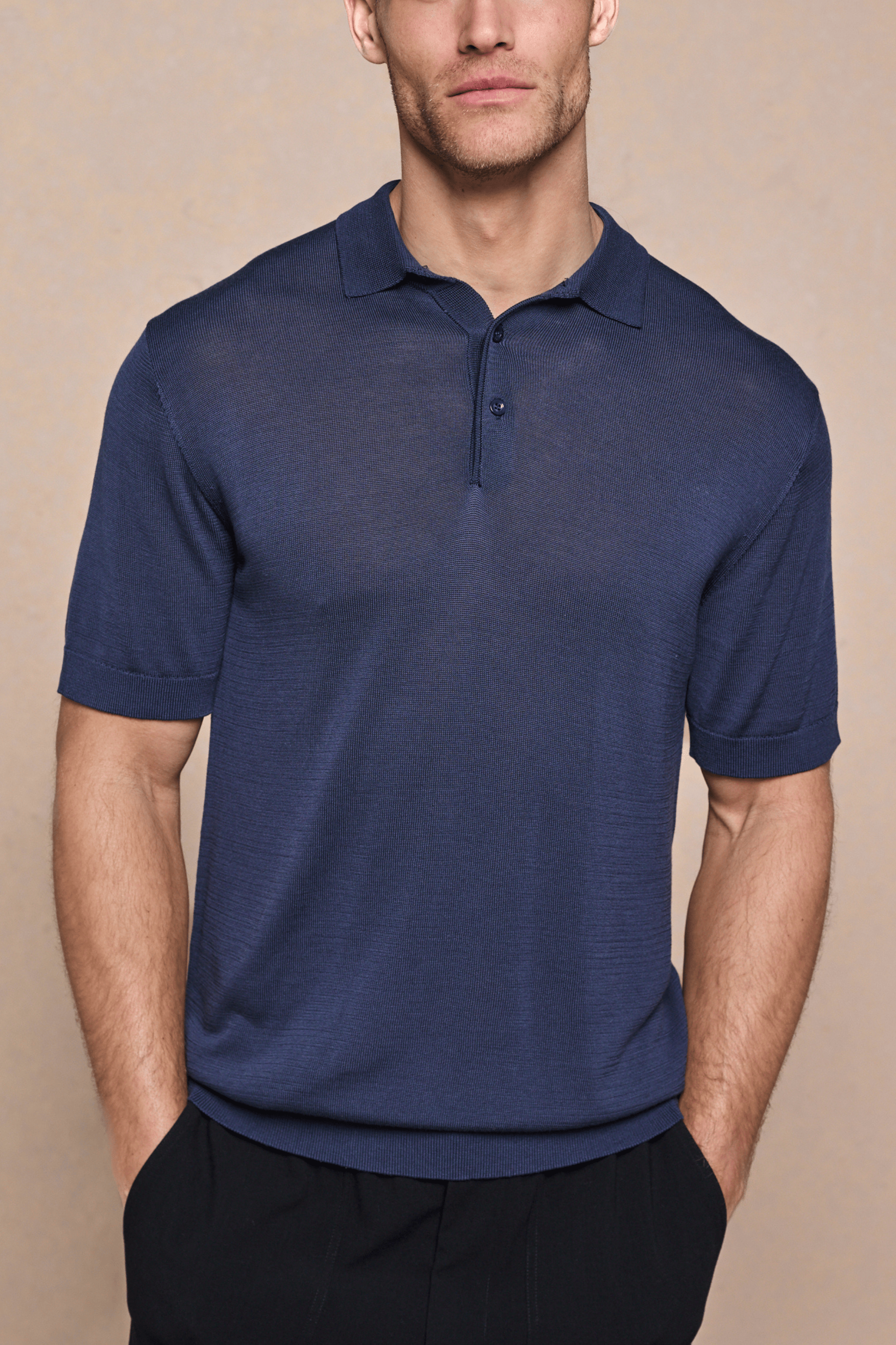Man wearing a navy knitted short sleeve polo with a half placket and ribbed details.