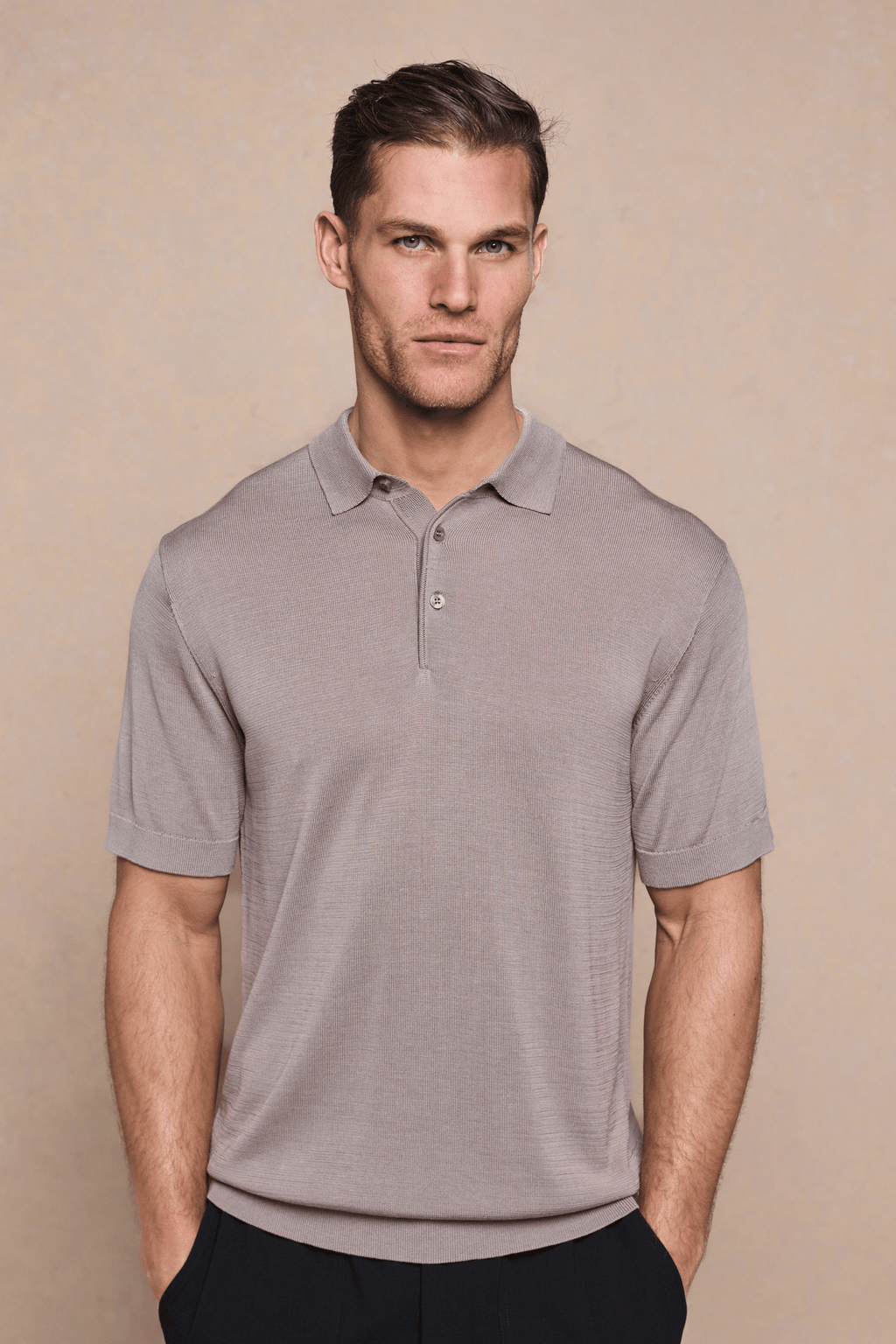 Man wearing a tailored sand knitted polo with a half placket, ribbed sleeves, and hem.