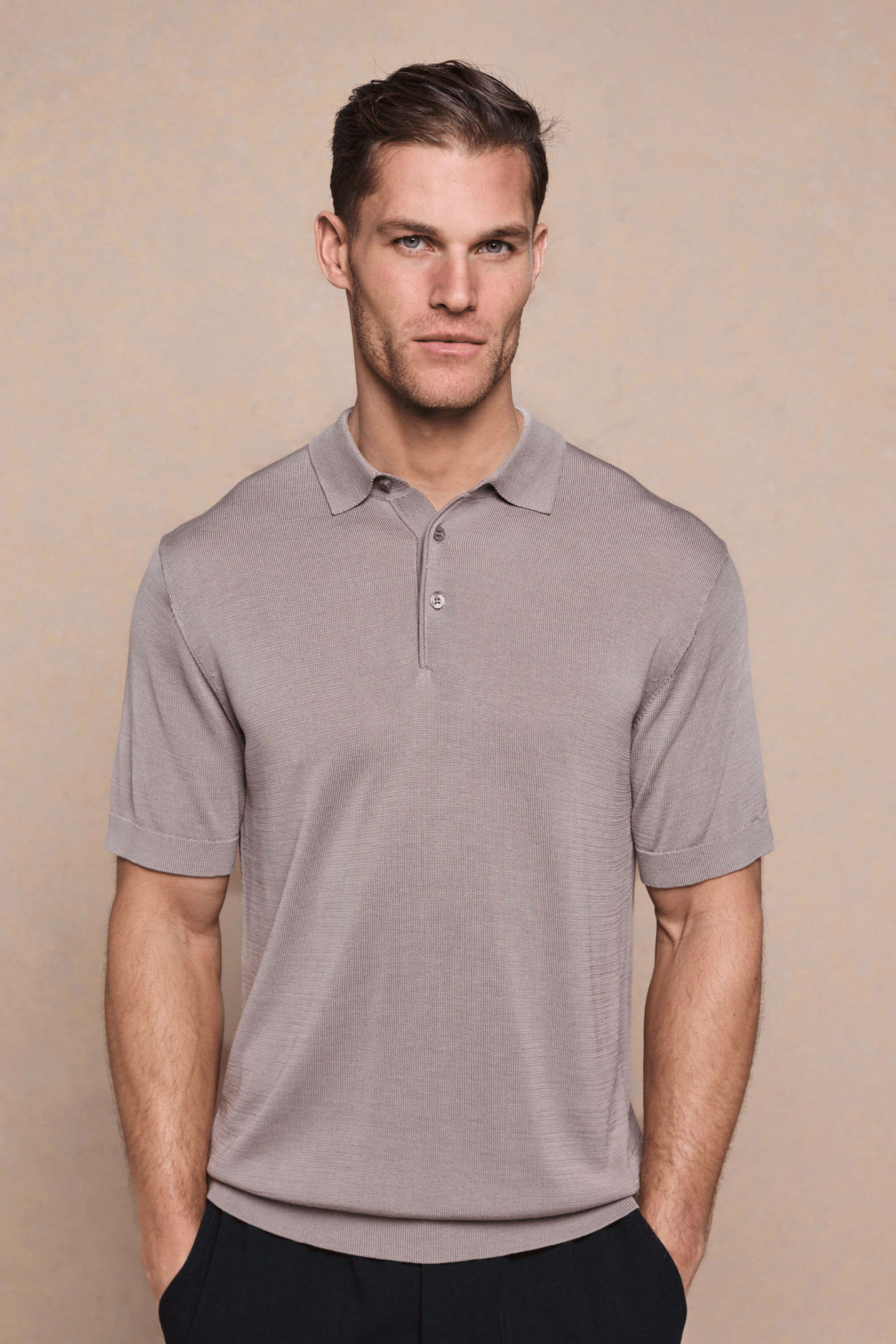 Man wearing a tailored sand knitted polo with a half placket, ribbed sleeves, and hem.