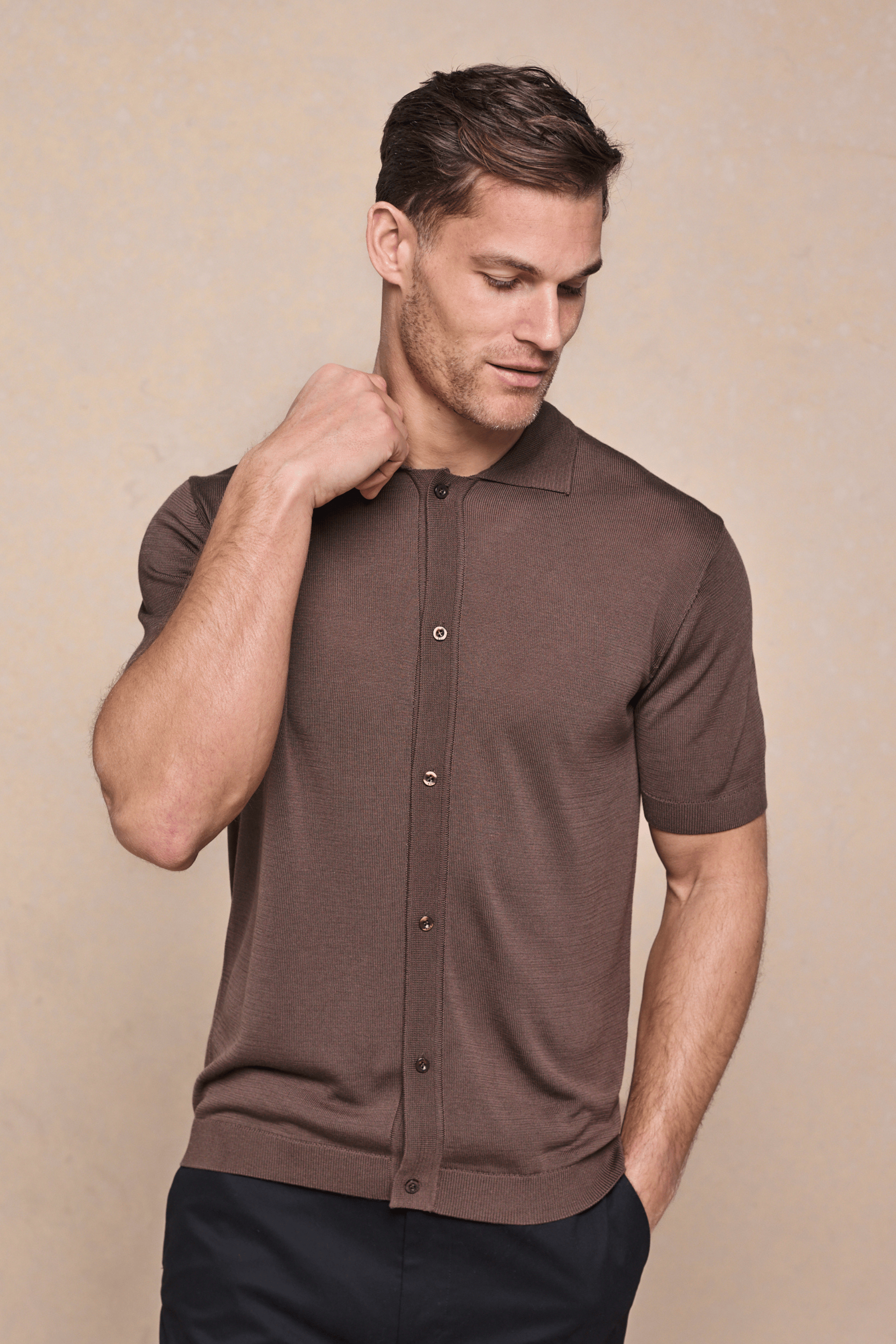 Man in a tailored brown knitted short-sleeve shirt with a full button-through front and ribbed details.