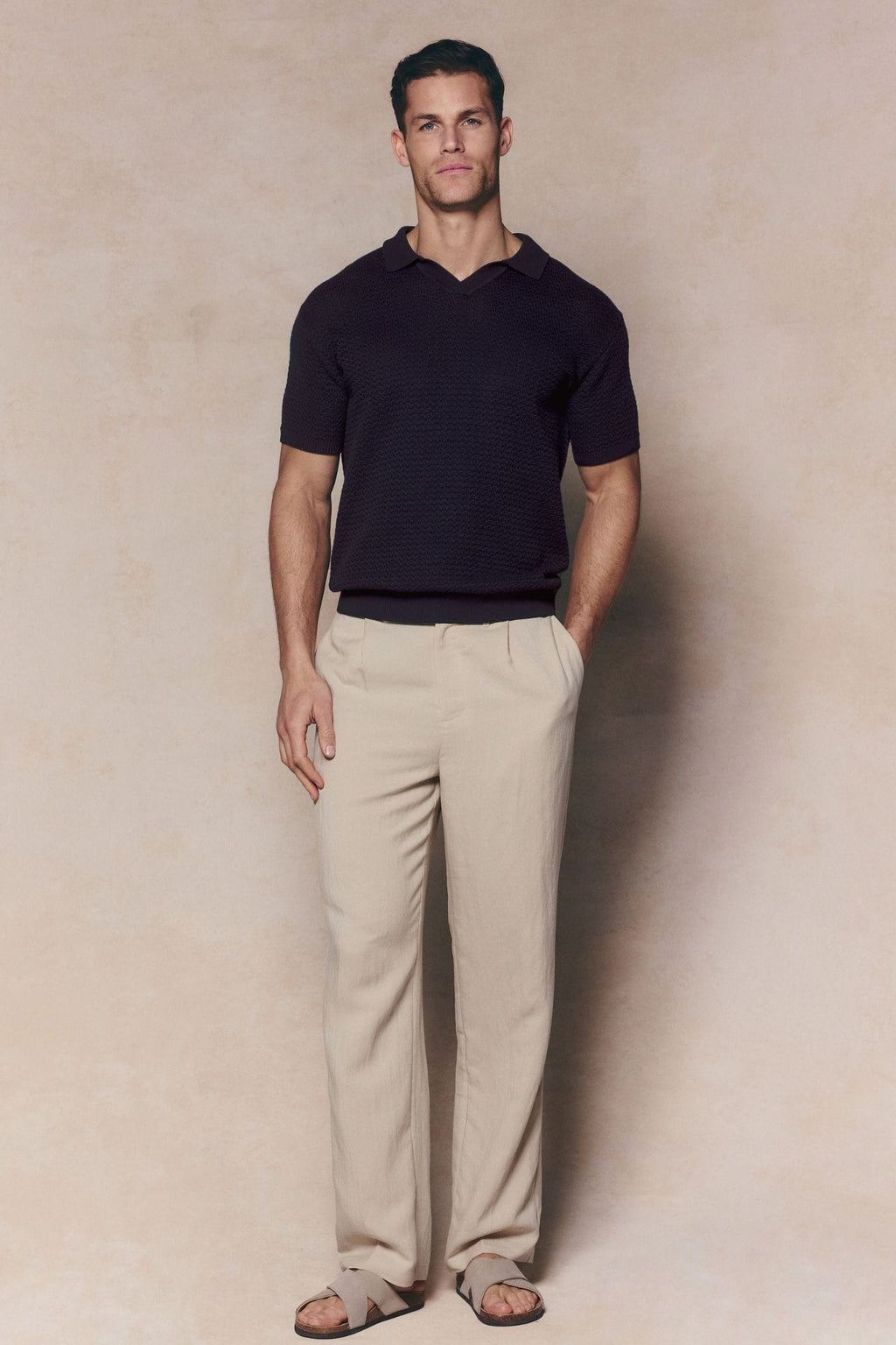 Man wearing a brown Rapha cotton knit polo with an open collar, ribbed hems, and light beige trousers.