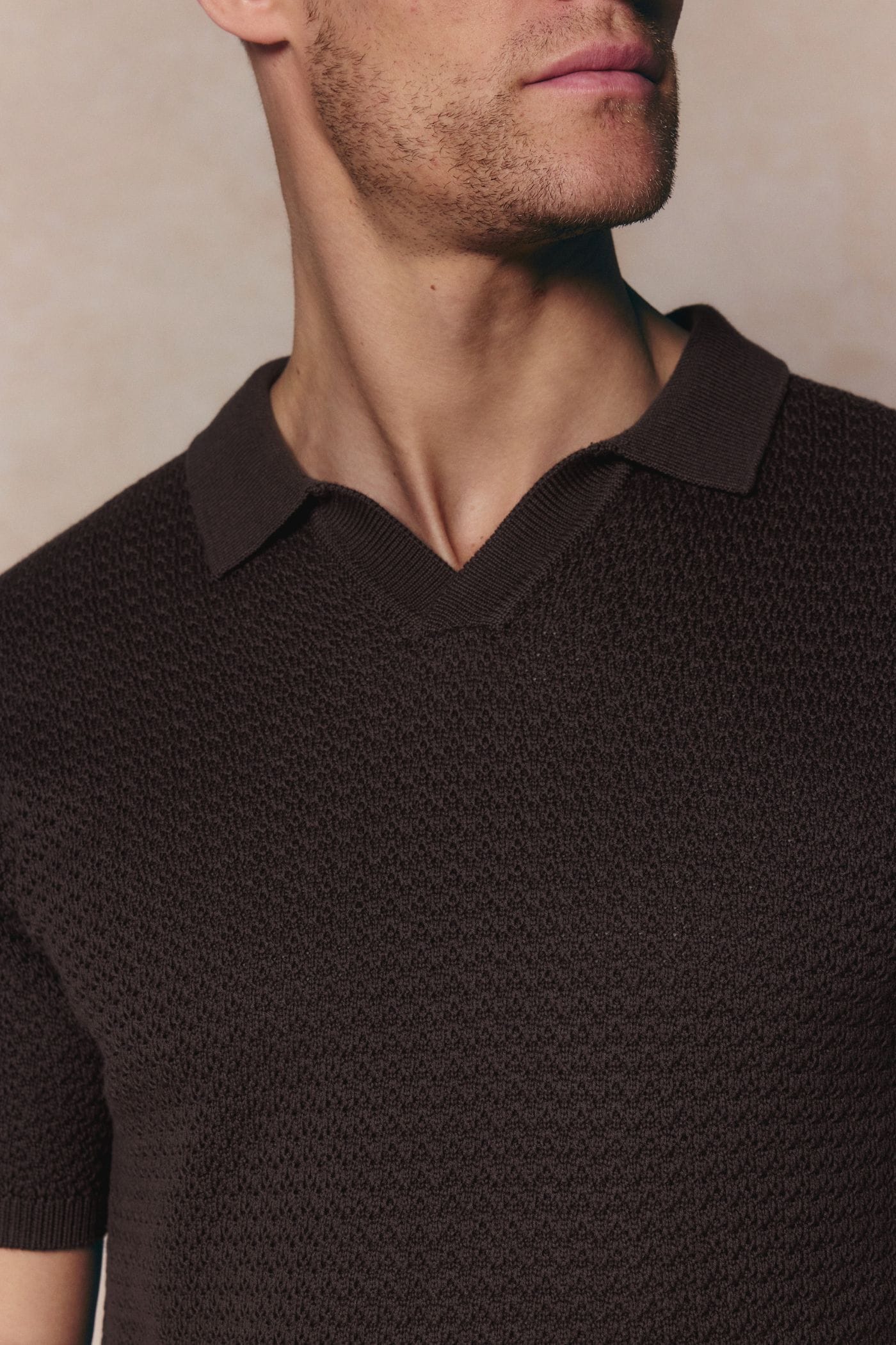 Close-up of a man wearing a brown Rapha Cotton Knit Polo with an open collar and textured finish.