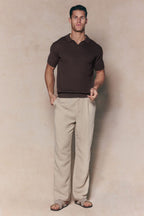 Man wearing a brown Rapha Cotton Knit Polo with an open collar, light beige pleated trousers, and sandals.