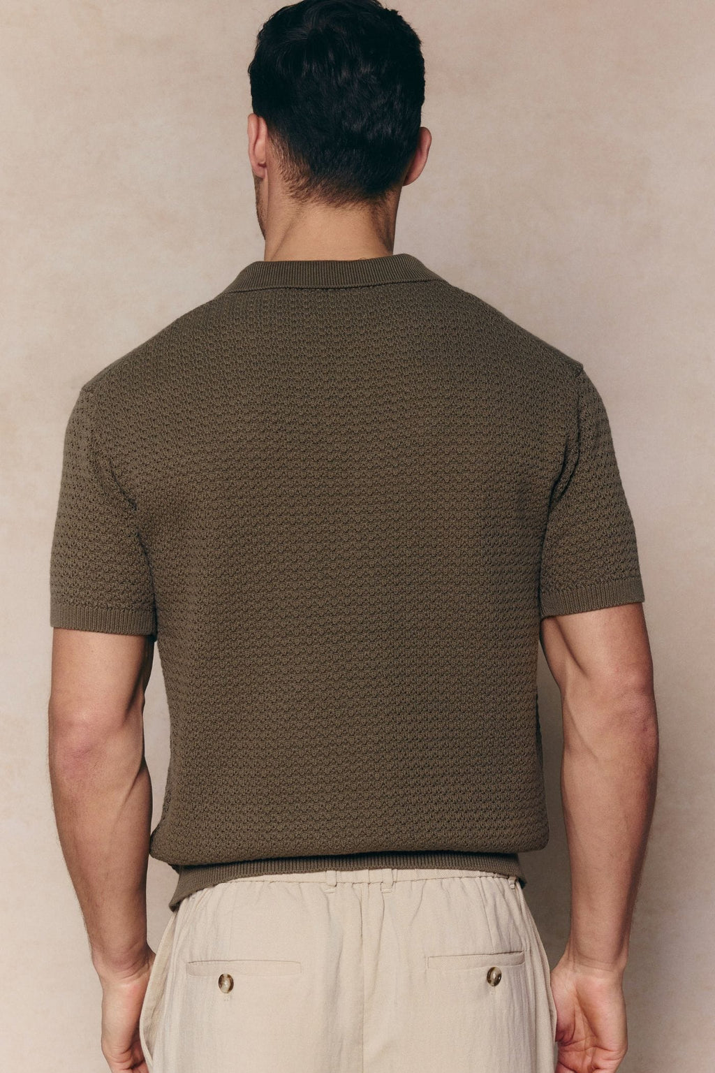 Man from behind wearing a dark olive Rapha cotton knit polo with textured finish and ribbed hem.