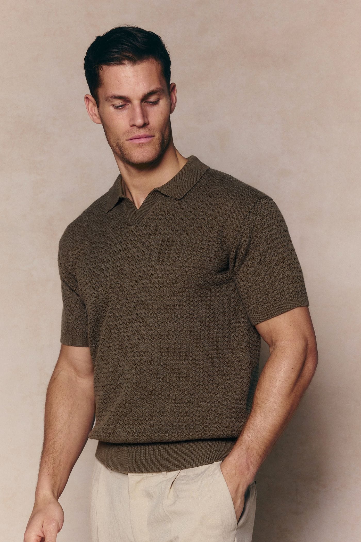 Man wearing a dark olive Rapha cotton knit polo with an open collar and ribbed hem, paired with light trousers.