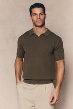 Man wearing a dark olive Rapha cotton knit polo with an open collar and ribbed hem, paired with light trousers.