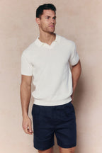Man wearing an ecru Rapha cotton knit polo with an open collar and navy shorts.
