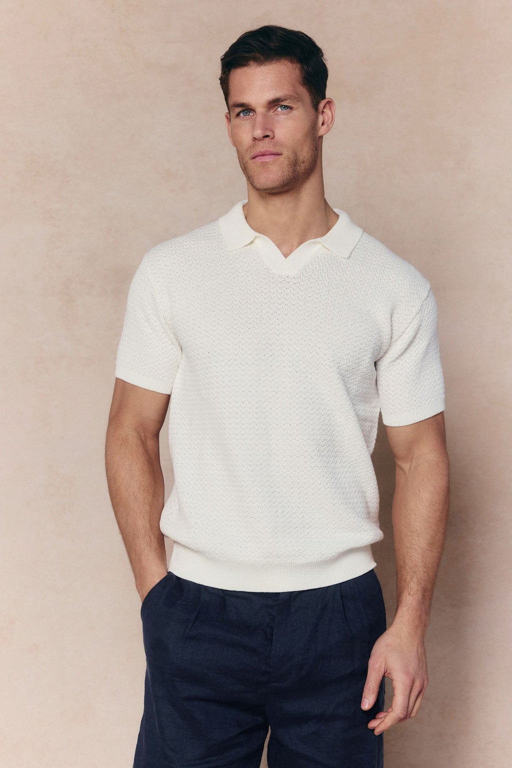 Man wearing an ecru Rapha Cotton Knit Polo with open collar, textured finish, and ribbed hems.