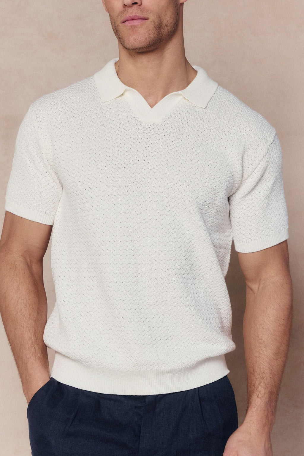 Man wearing an ecru Rapha Cotton Knit Polo with an open collar and textured finish, paired with navy trousers.