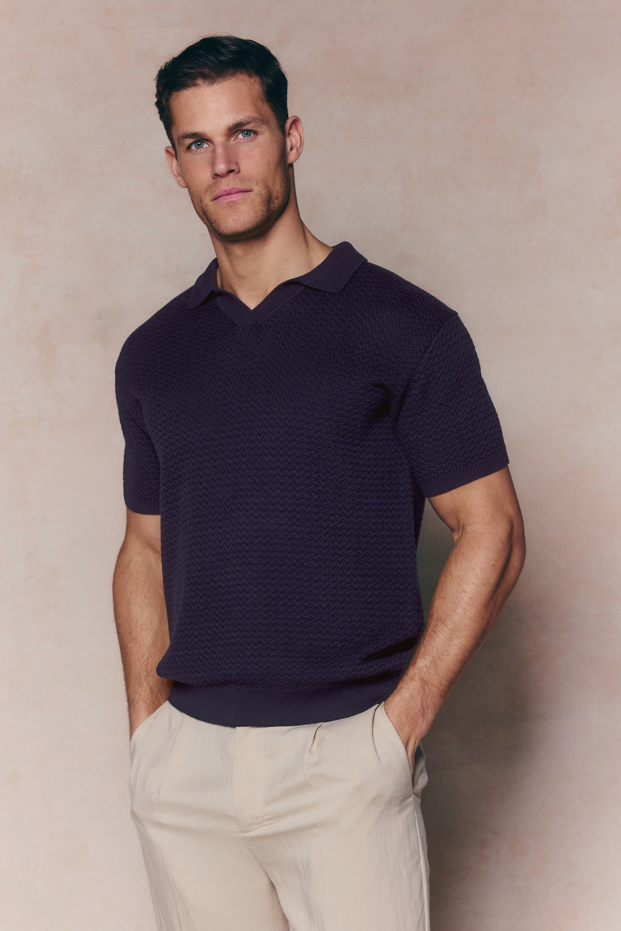 Man wearing a navy Rapha Cotton Knit Polo with an open collar and ribbed hem, paired with light trousers.