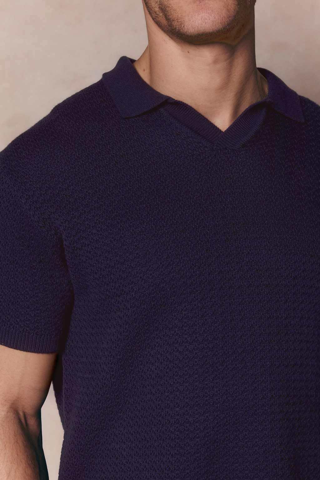 Close-up of a man wearing a navy Rapha Cotton Knit Polo with an open collar and textured finish.