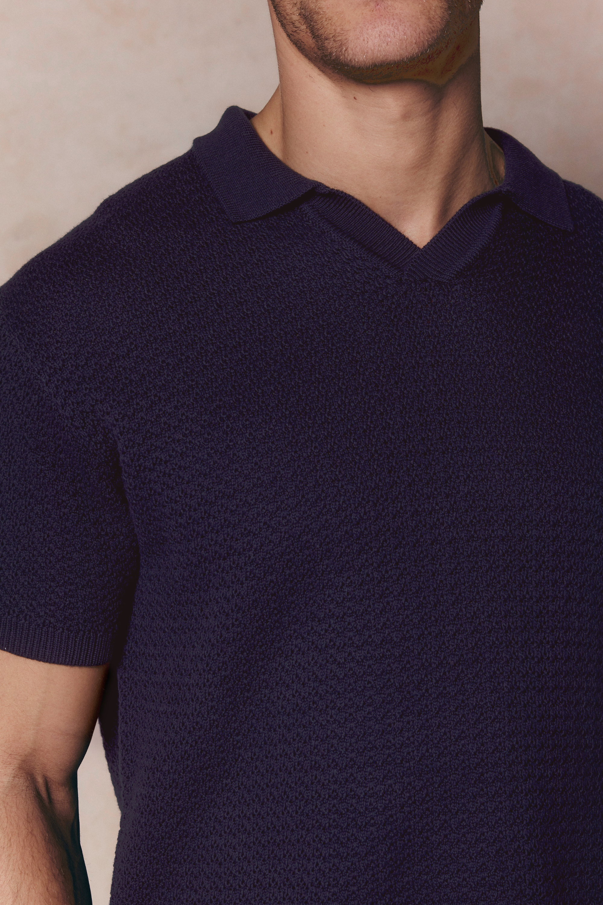 Close-up of a man wearing a navy Rapha Cotton Knit Polo with an open collar and textured finish.