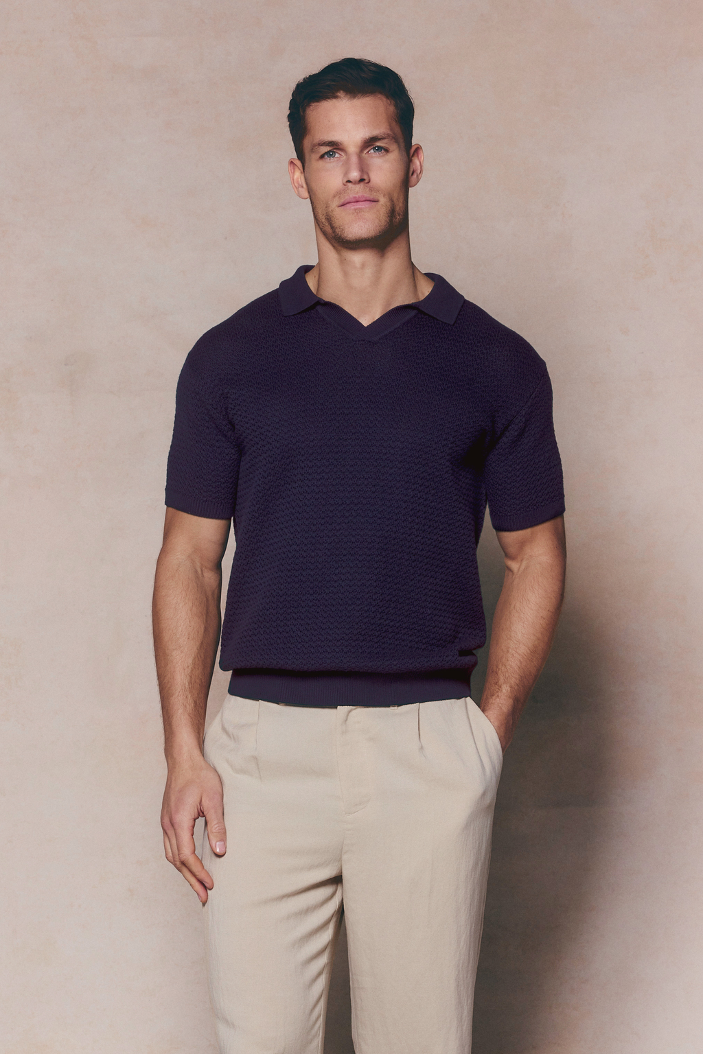 Man wearing a navy Rapha Cotton Knit Polo with an open collar and textured finish, paired with light trousers.