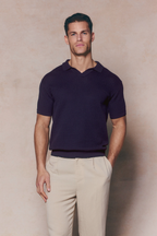 Man wearing a navy Rapha Cotton Knit Polo with an open collar and textured finish, paired with light trousers.