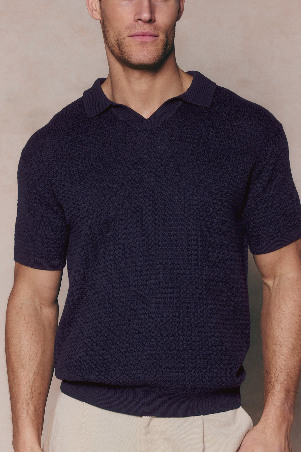 Man wearing a navy Rapha Cotton Knit Polo with an open collar and textured finish, paired with light trousers.