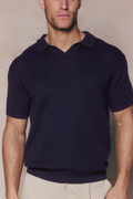 Man wearing a navy Rapha Cotton Knit Polo with an open collar and textured finish, paired with light trousers.