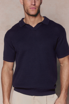 Man wearing a navy Rapha Cotton Knit Polo with an open collar and textured finish, paired with light trousers.