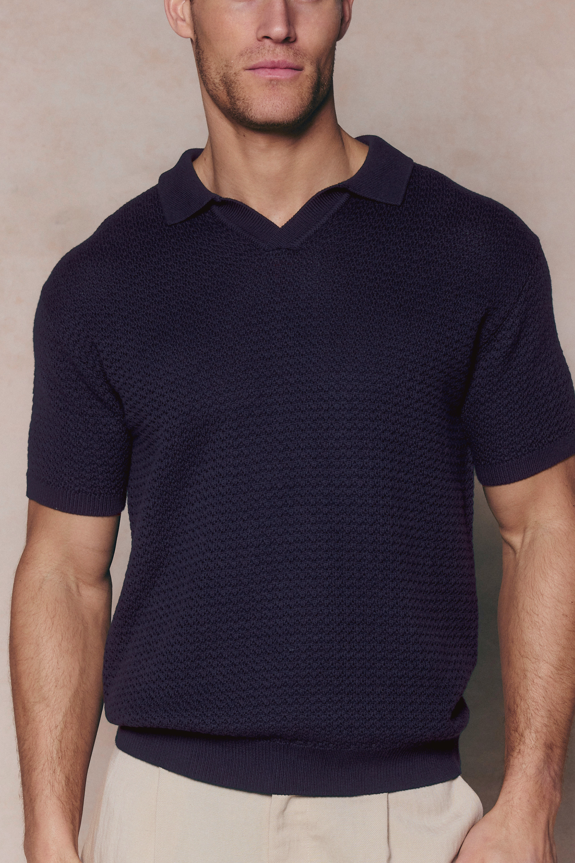 Man wearing a navy Rapha Cotton Knit Polo with an open collar and textured finish, paired with light trousers.