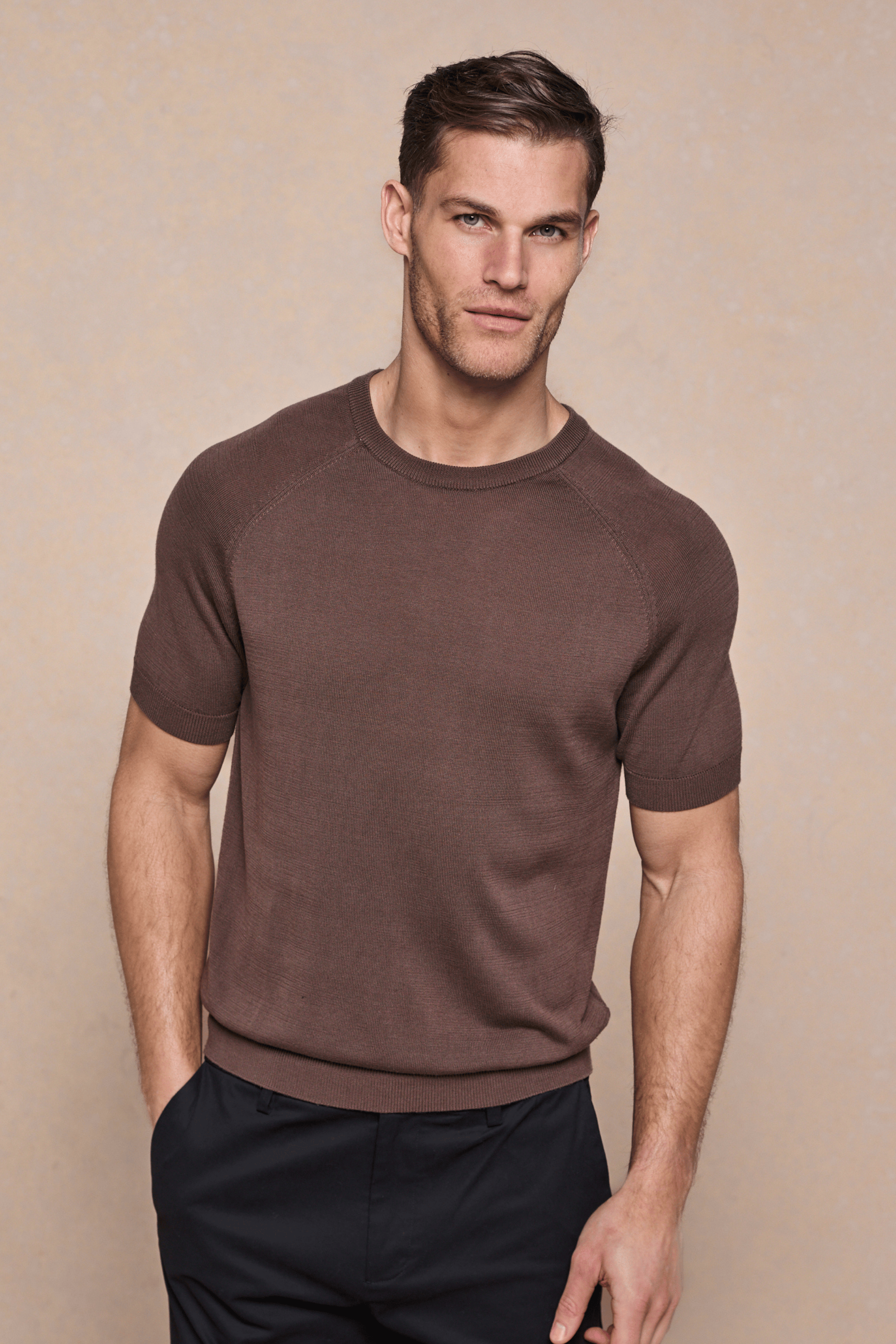 Man wearing a brown Riera Knit Crew Neck T-Shirt with ribbed details and black pants.
